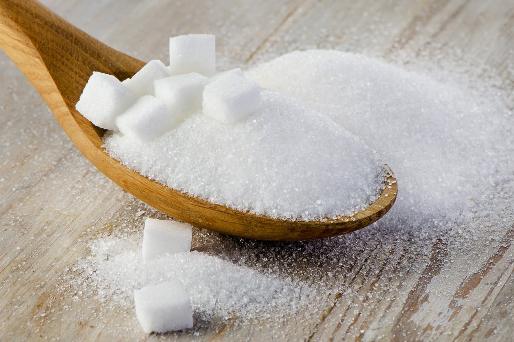 Spoon full of sugar on a wooden table, selective focus